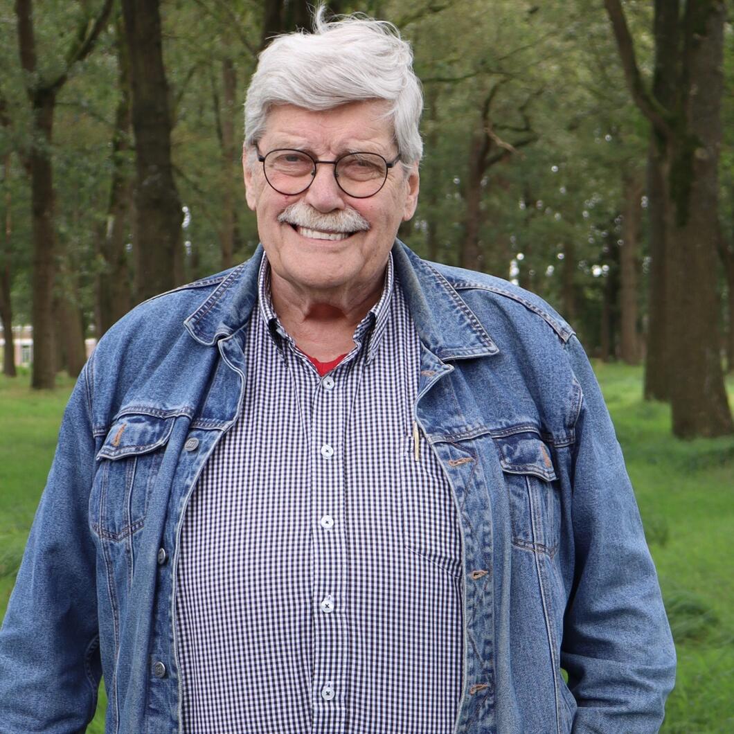 Fractielid Willem van der Meij draagt een blauw jasje en een blauwe blouse. Hij staat voor enkele bomen en op gras