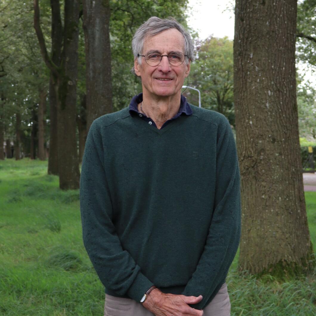 Fractielid Adriaan Ferf draagt een groene trui. Hij staat voor enkele bomen 