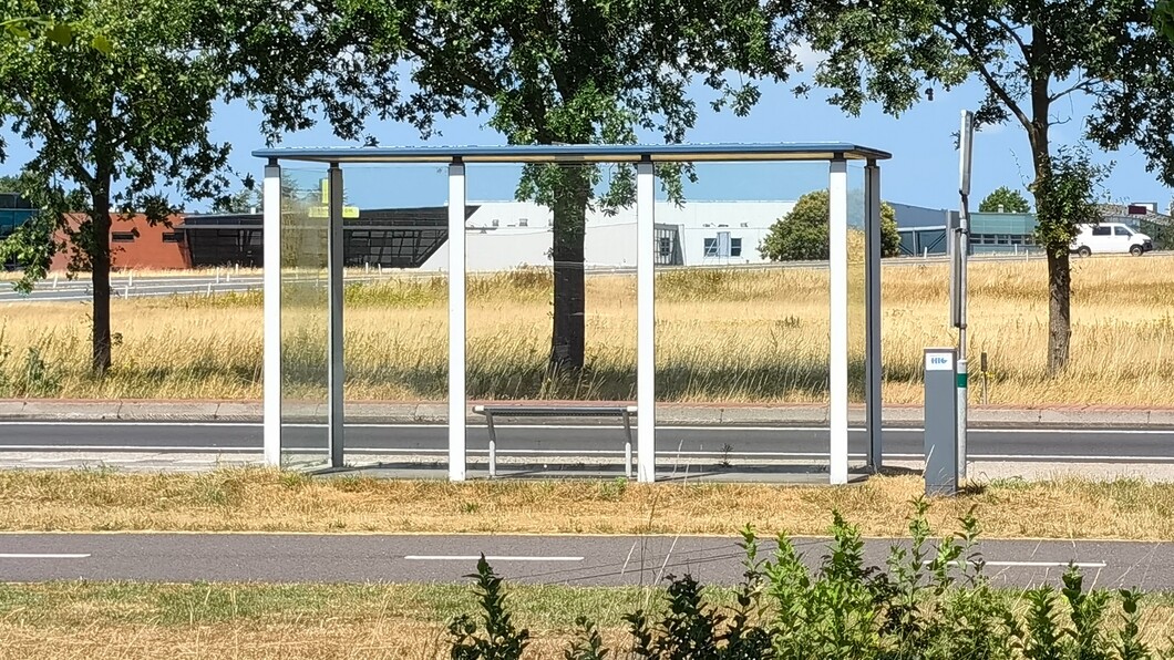 Bushalte bij Vriezerbrug. Op de achtergrond zijn wat bedrijfspanden te zien, met een autoweg