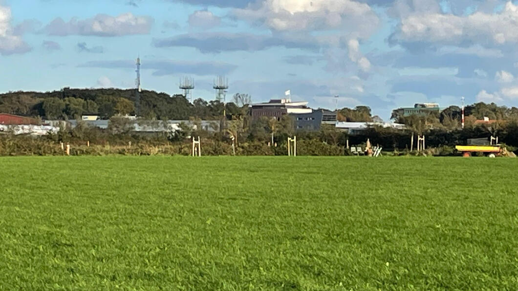 Een stuk groene landgoed met daarachter gebouwen van Groningen Airport Eelde