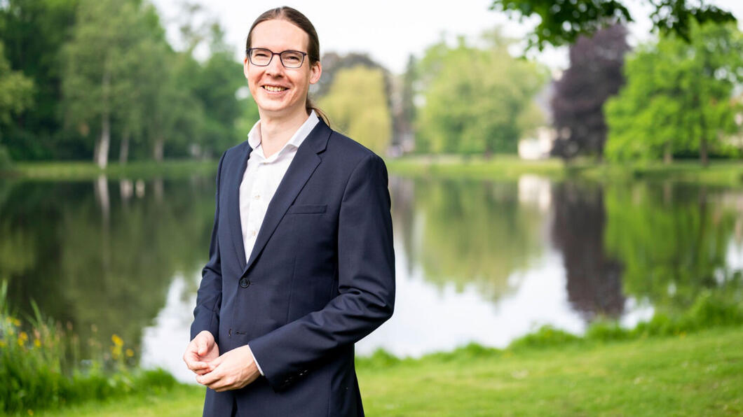 Hans Kuipers, onze nieuwe wethouder. Hans heeft een wit overhemd aan met een blauw/zwarte colbert. Op de achtergrond is een watertje te zien