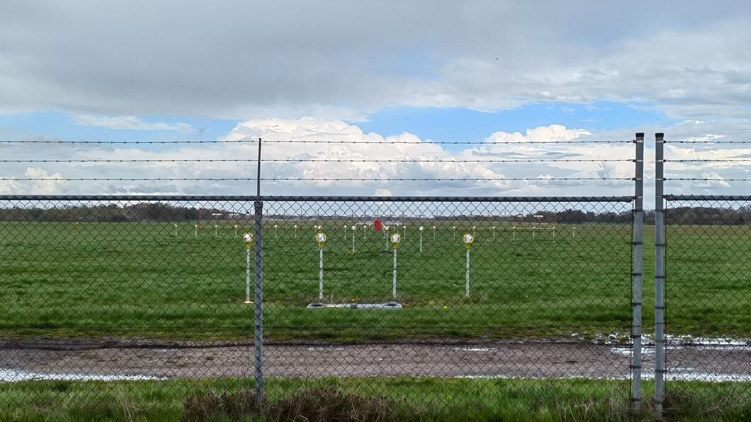 De verlichting van vliegveld Eelde. Het staat op een groen grasveld achter een bedraad hek met prikkeldraad