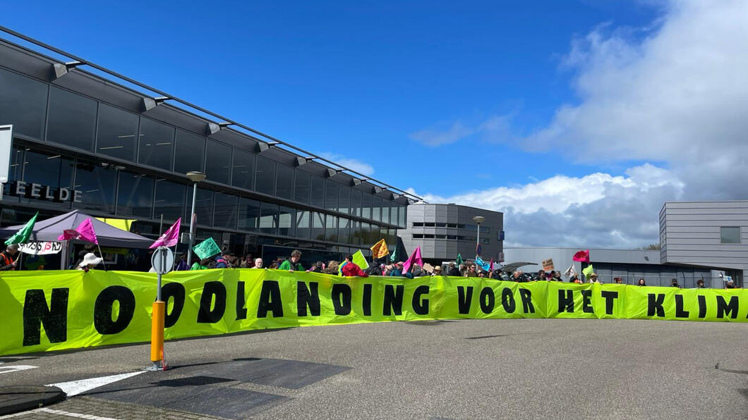 De demonstratie bij vliegveld Eelde. Met ruim 100 anderen stonden we voor het vliegveld. We houden een spandoek vast met daarop 'noodlanding voor het klimaat'.