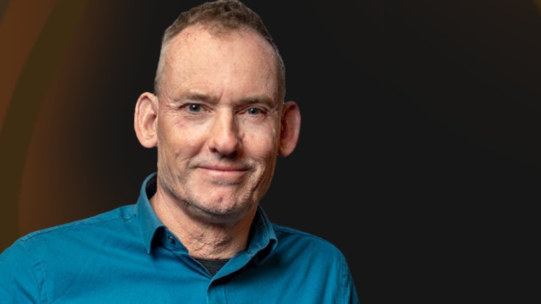 Robert de Jonge, de nieuwe voorzitter van GroenLinks. Hij staat voor een donkerbruine achtergrond en heeft een lichtblauwe polo aan