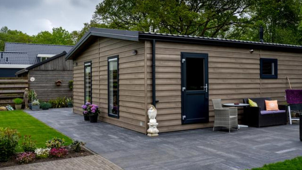 Een pre-mantelzorgwoningen. Met op de achtergrond bomen vol in blad en rondom de woning liggen grijze tegels