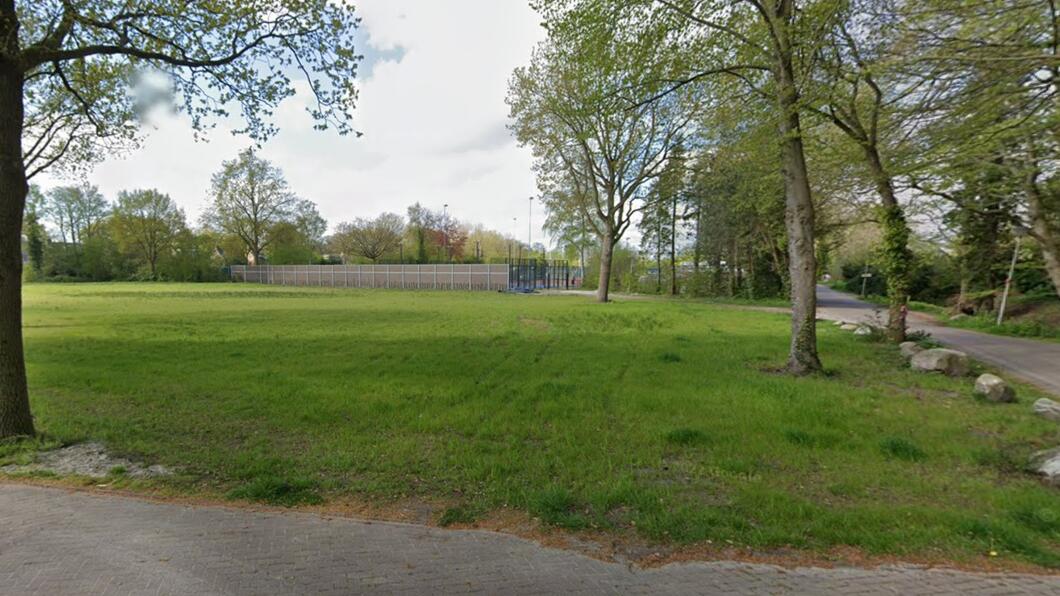 Het terrein van voormalig sporthal De March. Een groen grasveld met enkele bomen
