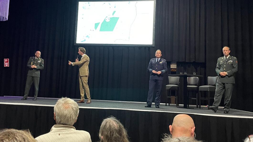 De bijeenkomst. 4 mensen van onder andere het ministerie en van Defensie op een podium