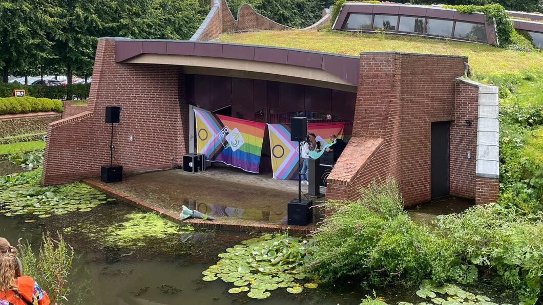 Een gecreëerd podium in Museum de Buitenplaats. Voor het podium ligt een vijvertje, op het podium staan enkele Pride vlaggen