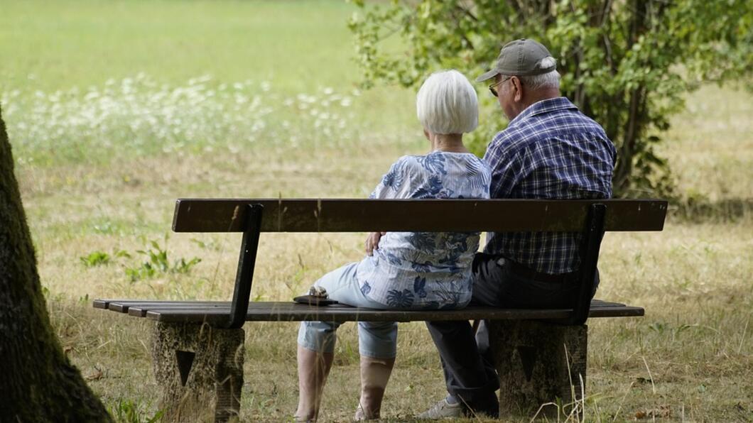 Ouderen: Twee mensen op leeftijd zitten samen op een bankje te kijken naar een grasveldje