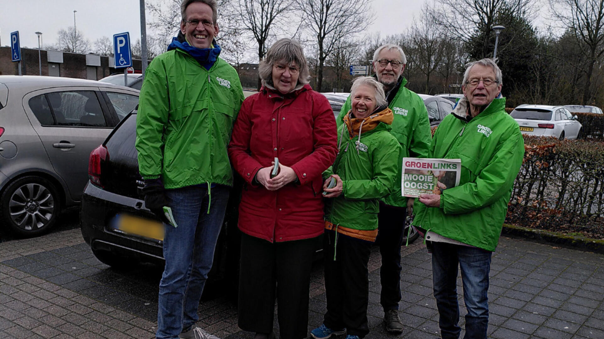 Vijf leden van ons campagneteam op een parkeerplaats. De leden hebben groene jassen aan