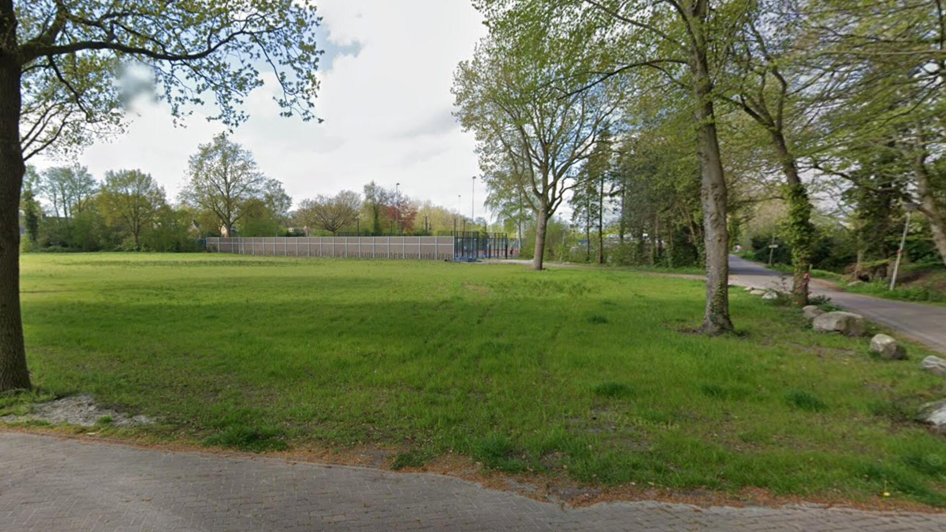 Het terrein van voormalig sporthal De March. Een groen grasveld met enkele bomen