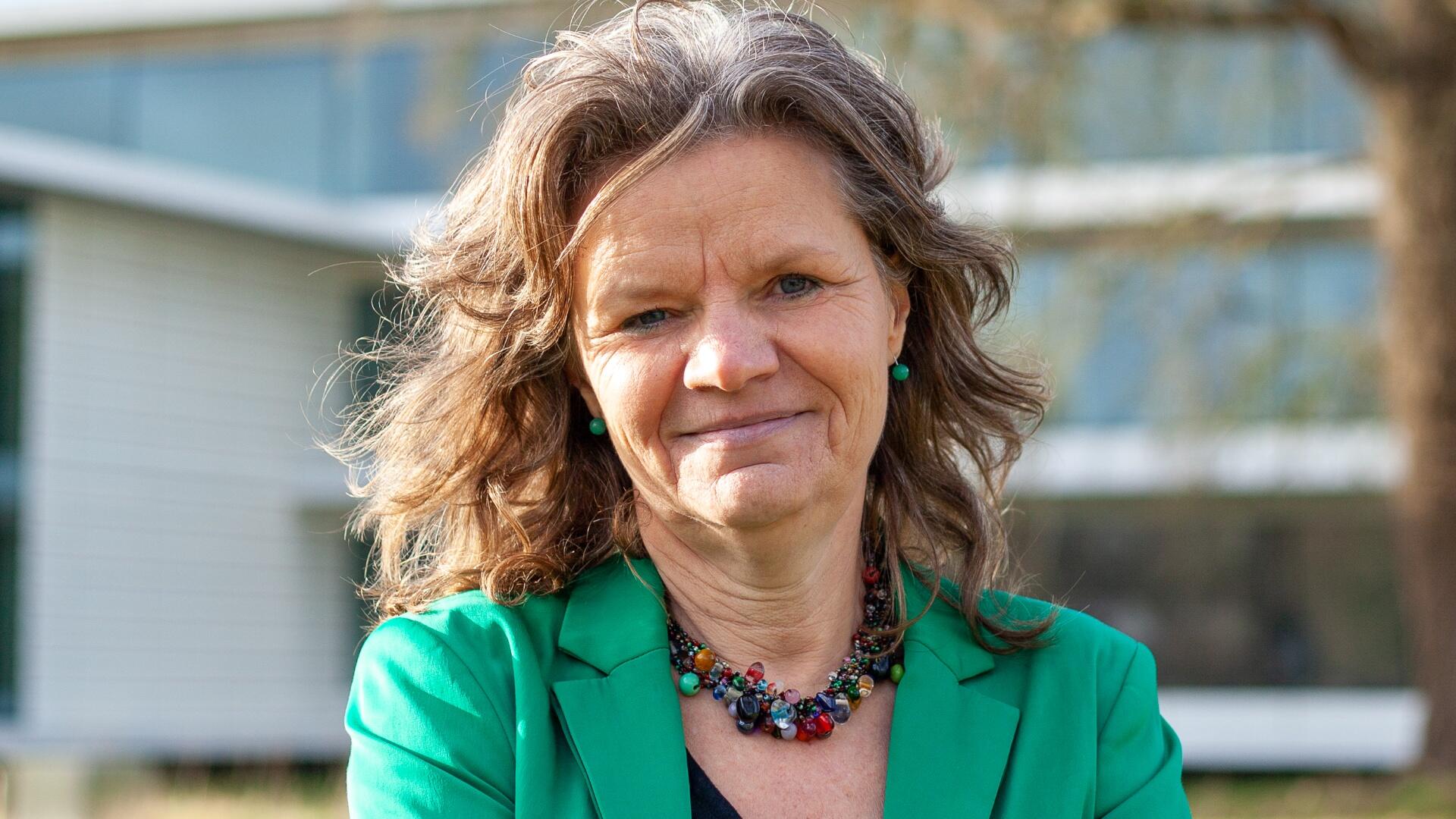 Gea Bijkerk, onze fractievoorzitter. Gea draagt een groen jasje en staat voor het gemeentehuis
