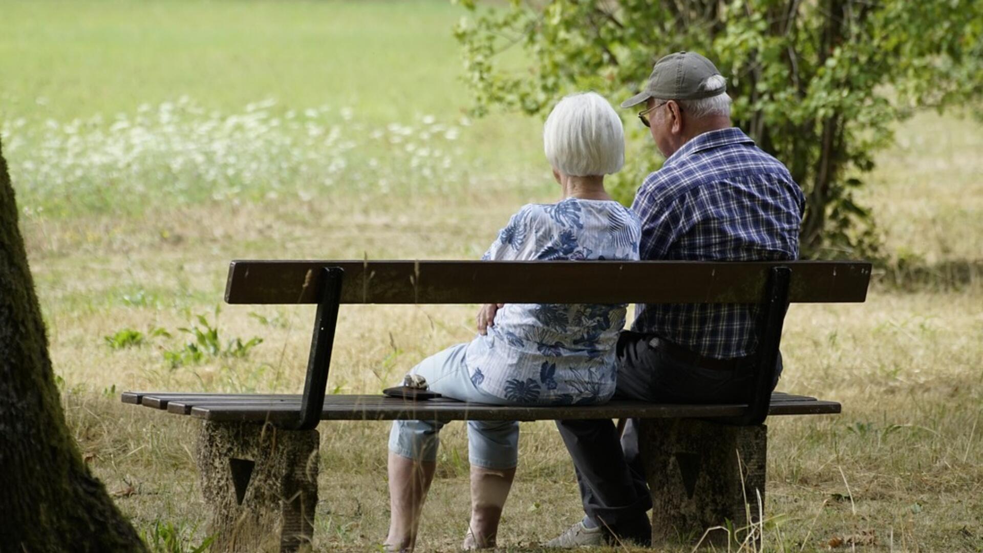 Ouderen: Twee mensen op leeftijd zitten samen op een bankje te kijken naar een grasveldje