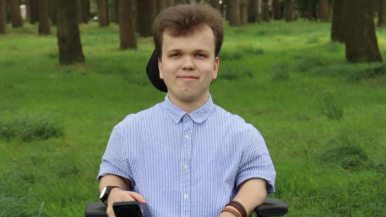 Tim Paul Ploeger, commissielid van GroenLinks Tynaarlo, zittend in zijn rolstoel voor wat begroeiing